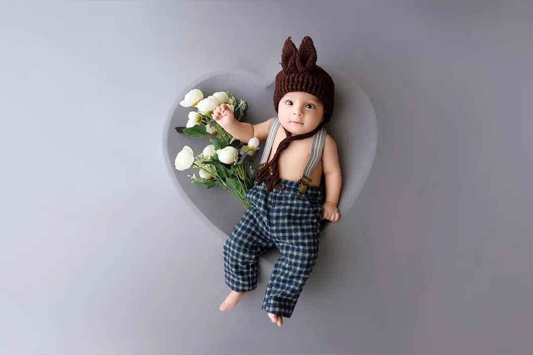 A baby lying in a heart-shaped tub with flowers, wearing a cute dress, captured during an adorable baby photoshoot.